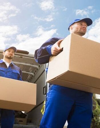 Close-up Of Two Young Delivery Men Carrying Cardboard Box In Front Of Truck